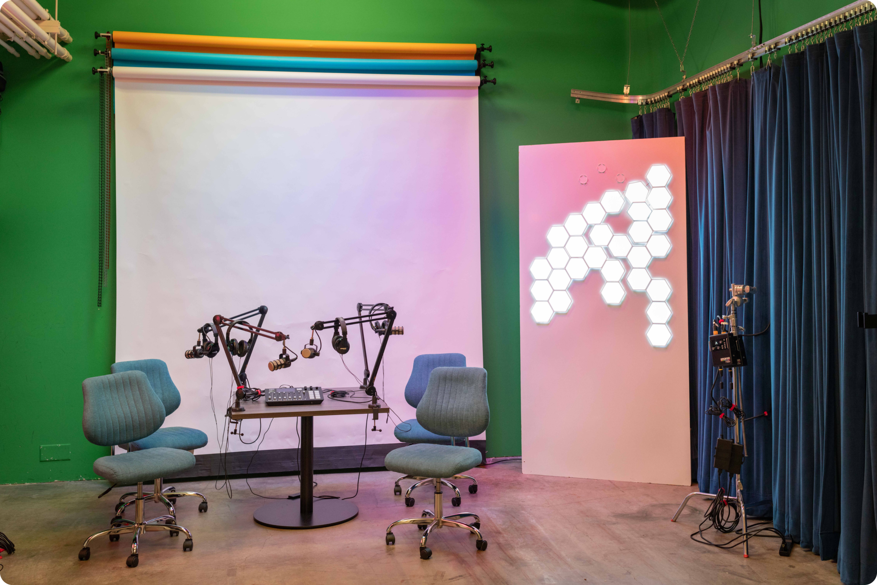 photo shows de neve studios lit up with hexagonal LEDs. There are hues of red and violet over everything. There is a podcast setup in the midle of the room