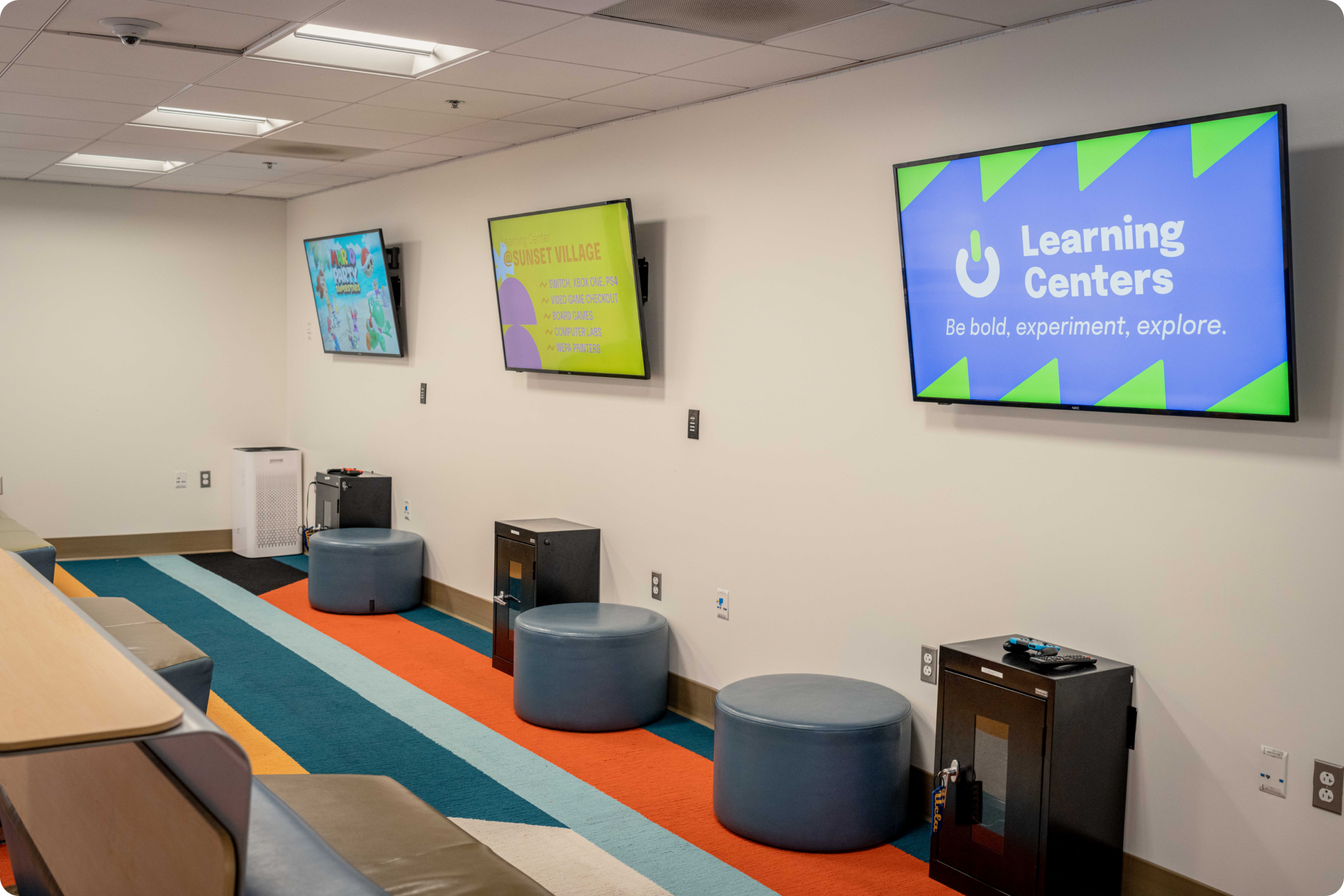 pictured is sunset village learning centers with a rainbow style pastel carpet, TVs, a front desk and more