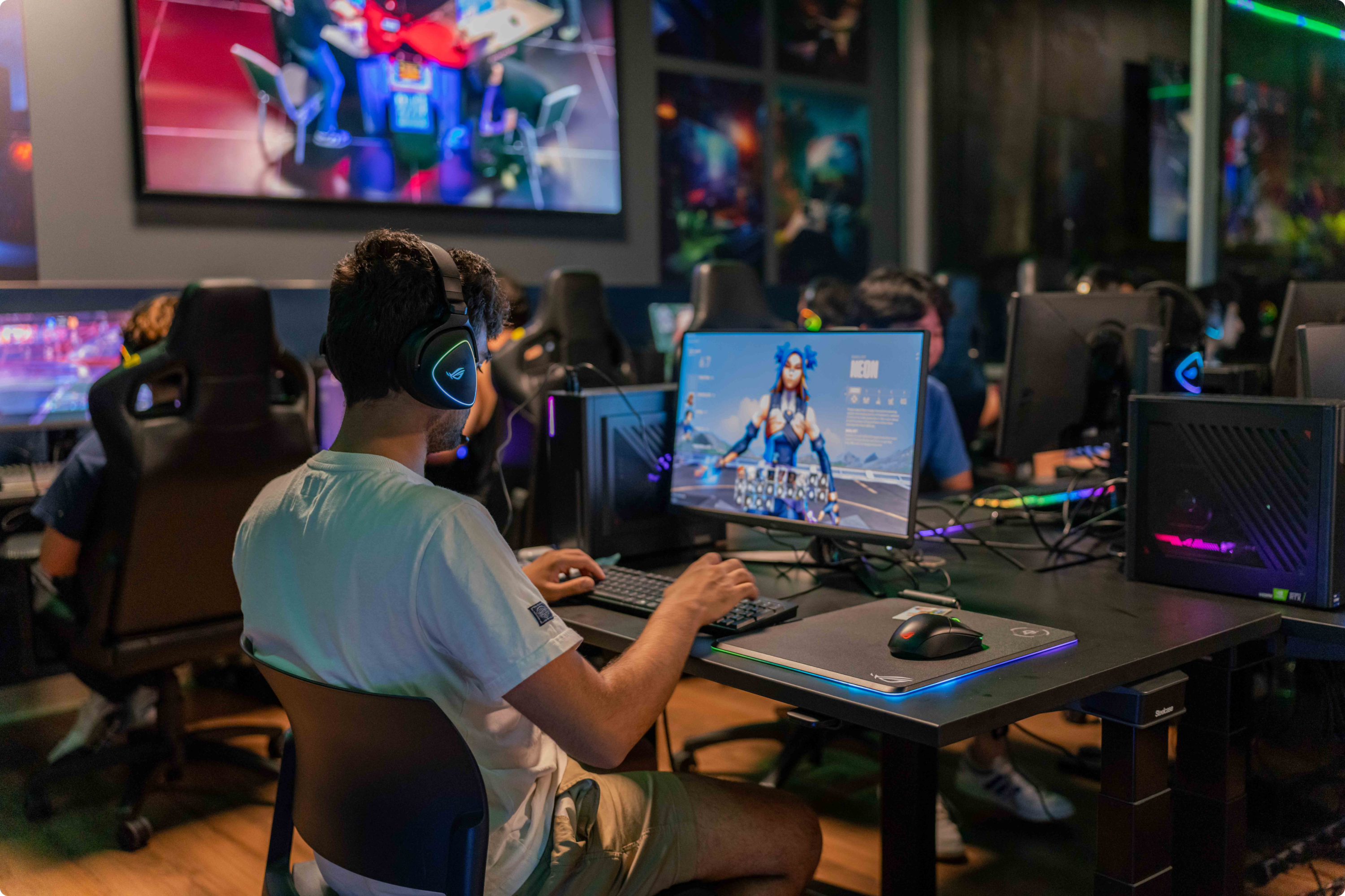 picture shows an individual playing games on a gaming pc while the background is filled with other student doing the same