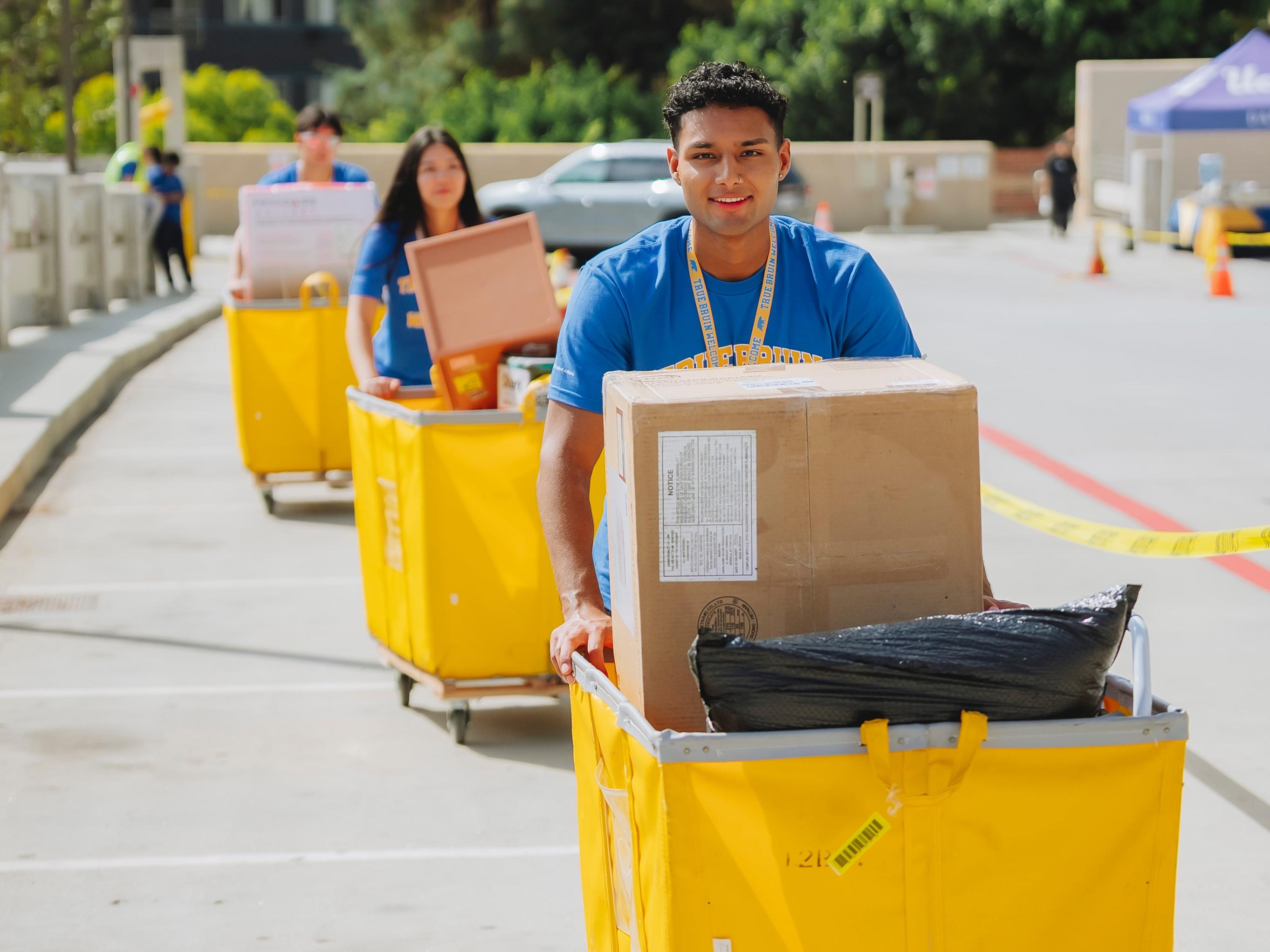 Student in True Bruin Welcome shirt pushing yellow move in cart.
