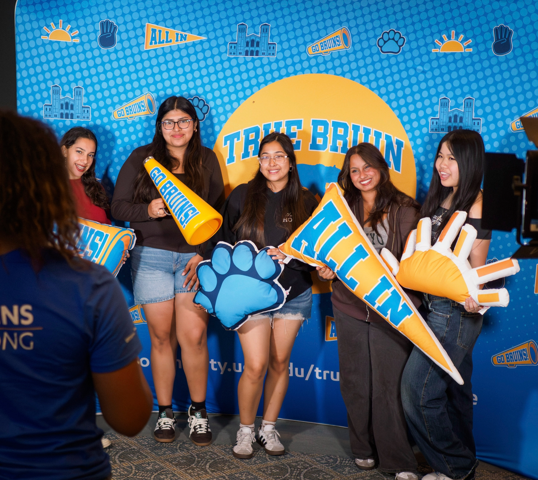Photo of student taking a photo of group of students holding True Bruin Welcome pillow props.