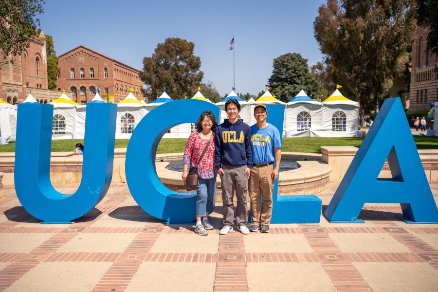 Student and parents standing in front of UCLA letters.