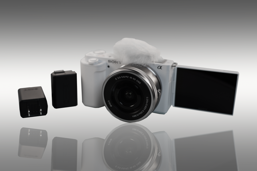 picture shows a sony camera with a battery and memory card. The camera has its screen flipped out and it white with a gray to white then gray gradient vertically